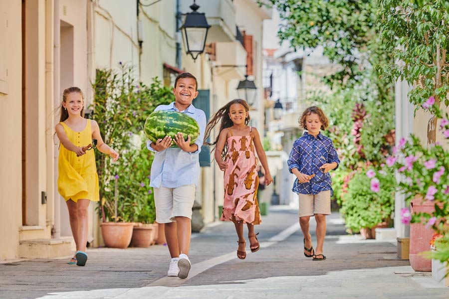 4 børn på ferie kommer bærende på en vandmelon i en lille gade